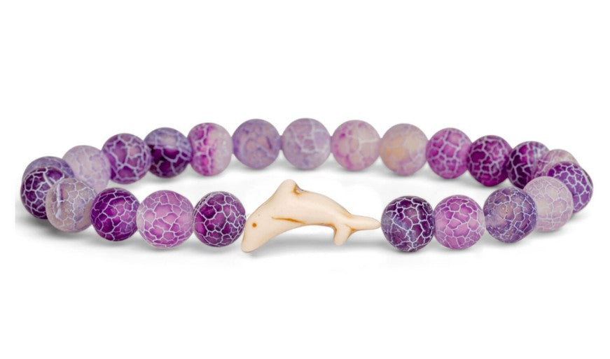 The fahlo Odyssey - Coral Reef Violet Dolphin bracelet features round purple and white marbled beads with a central beige dolphin-shaped bead—an ideal accessory for marine conservation enthusiasts.