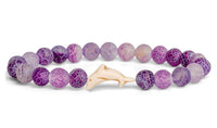 The fahlo Odyssey - Coral Reef Violet Dolphin bracelet features round purple and white marbled beads with a central beige dolphin-shaped bead—an ideal accessory for marine conservation enthusiasts.