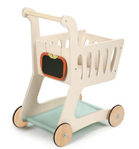 The Tenderleaf Shopping Cart by Tenderleaf features a light-colored wooden frame, four wooden wheels, a chalkboard apple sign in front, and a light blue fabric shelf—ideal for imaginative play and carrying pretend groceries.