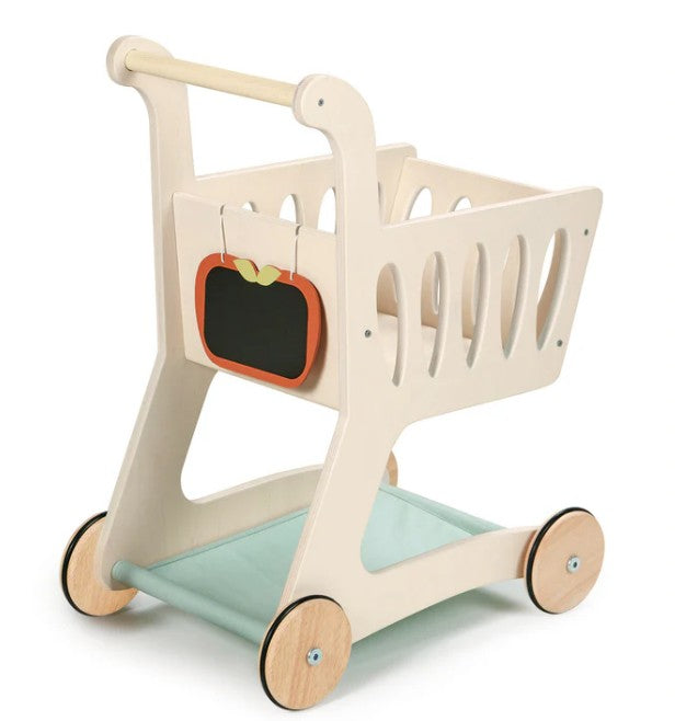 The Tenderleaf Shopping Cart by Tenderleaf features a light-colored wooden frame, four wooden wheels, a chalkboard apple sign in front, and a light blue fabric shelf—ideal for imaginative play and carrying pretend groceries.