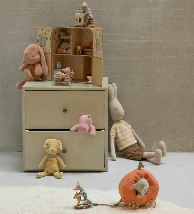 A children’s room scene with a beige dresser, toy animals—a rabbit, bear, pink pig, and the Maileg Pumpkin Carriage, Mouse by Maileg—plus a miniature dollhouse arranged for imaginative storytelling against a neutral wall and carpet.