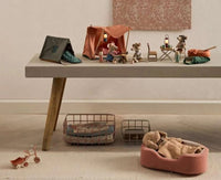 A tabletop features the Maileg Happy Camper Tent, Mouse and accessories for imaginative play. Below, a toy tricycle, baskets, and a toy animal in a pink bed complete this cozy camping scene.