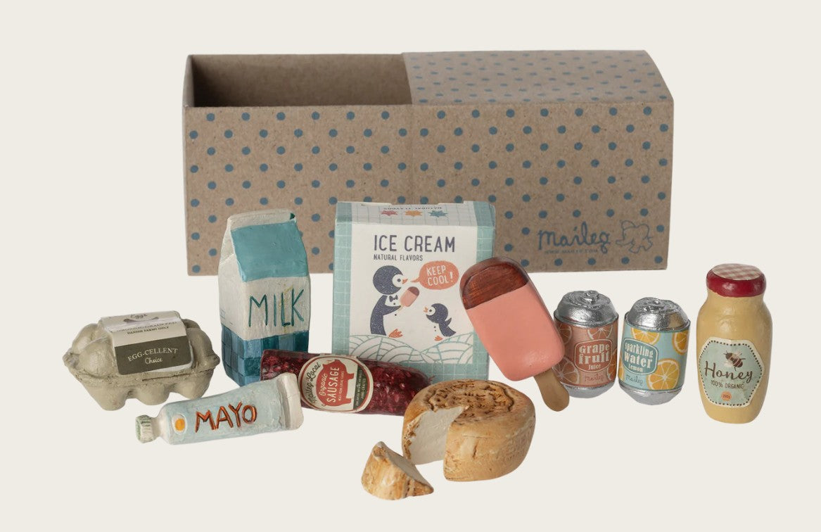 The Maileg Grocery Box, Miniature includes tiny groceries like eggs, milk, and ice cream, all displayed in front of a brown box with blue polka dots and the Maileg brand name—perfect for imaginative play.