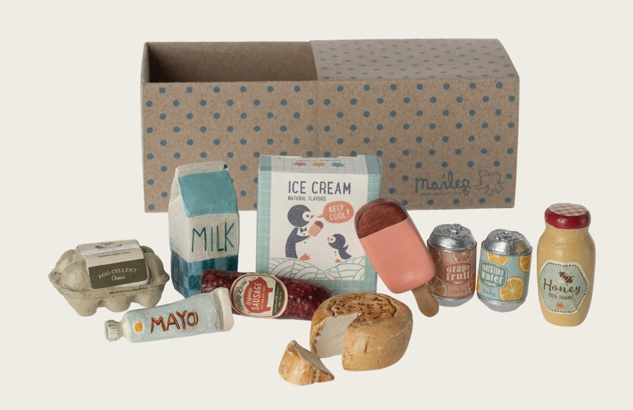 The Maileg Grocery Box, Miniature includes tiny groceries like eggs, milk, and ice cream, all displayed in front of a brown box with blue polka dots and the Maileg brand name—perfect for imaginative play.