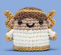 Claire the Angel Crochet Kit by The Woobles features a brown-haired, golden-winged angel with a white body and smiling face—set against a light blue background, it’s perfect for your crochet starter or beginner kit projects.