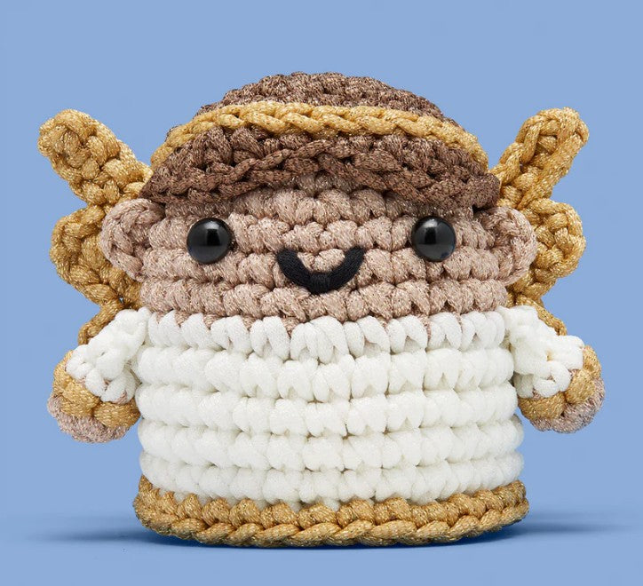 Claire the Angel Crochet Kit by The Woobles features a brown-haired, golden-winged angel with a white body and smiling face—set against a light blue background, it’s perfect for your crochet starter or beginner kit projects.