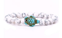 The Journey - White Howlite Turtle bracelet by fahlo features round white howlite beads and a turquoise turtle charm—displayed on a white background, it's perfect for supporting marine conservation.