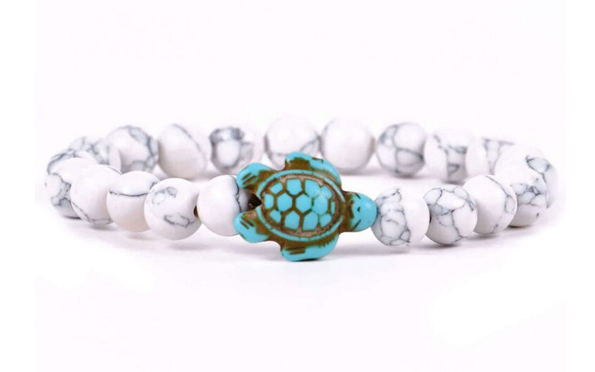 The Journey - White Howlite Turtle bracelet by fahlo features round white howlite beads and a turquoise turtle charm—displayed on a white background, it's perfect for supporting marine conservation.