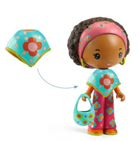 Meet DJECO Tinyly Poppy & Nouky—a charming collectible figure from DJECO featuring Poppy, a figurine with brown skin and curly brown hair dressed in a pink outfit decorated with blue and orange flower patterns, yellow earrings, a coordinating blue purse, and a removable blue cape adorned with flowers. Perfect for imaginative play or adding to your Tinyly collection!.