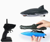 Held by two hands on a white background, the CrocSharkboat R/C 2.4G from Jupiter Creations, Inc., along with a toy shark and a black remote control, invite adventurous play with this blue remote-control vehicle featuring an alligator head attachment.