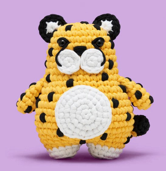 Suri the Cheetah Crochet Kit by The Woobles features a soft, crocheted yellow cheetah with black spots, round ears, black eyes, and a white snout—perfect for inspiring your next beginner crochet animal project.