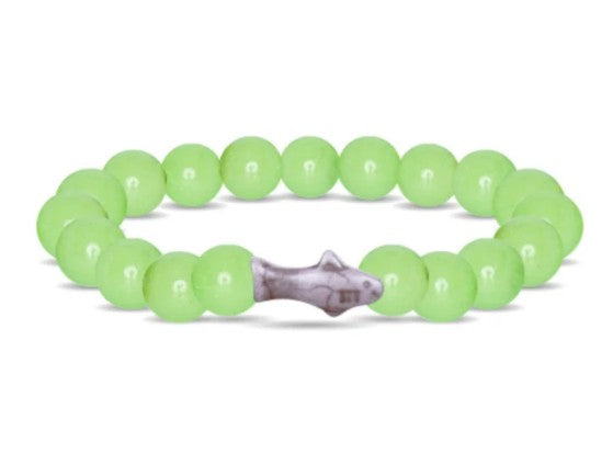 The fahlo Voyage - Sage Glow Shark is a stretchy, glow-in-the-dark bracelet made of round, light green beads with a unique shark-shaped centerpiece.
