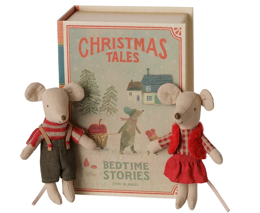 Two Maileg Christmas twin mice, Little sister and brother, dressed in festive outfits, sit in front of a book-shaped box titled “Christmas Tales: Bedtime Stories,” adorned with wintery illustrations—a charming holiday gift from Maileg, perfect for the season.