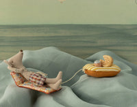 Maileg Beach Mouse With Air Mattress, Dad - Flower by Maileg features Dad Mouse lounging in plaid shorts on a patterned chair, with a string-attached yellow air mattress, creating a playful summer beach scene against a soft, fabric-like background.