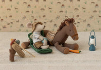 A plush mouse in camping clothes sits on a sleeping bag next to a plush horse with a carrot. Beside them is the Maileg Vintage Lantern, Mouse - Blue by Maileg and a turtle on crutches with a backpack, all set against a desert backdrop.