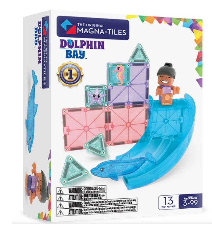 The Magna-Tiles Dolphin Bay 13-Piece Set by Magna-Tiles features ocean-themed magnetic building tiles, including pieces shaped like a dolphin and a pink star, as well as a smiling child figure on a blue slide. Designed for ages 3–99.