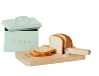 A wooden cutting board with a knife and bread sits before a Maileg Bread Box W. Utensils, Miniature—ideal for charming your Maileg Mouse furniture or miniature kitchen accessories collection.