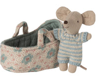 The Maileg Baby Mouse In Carry Cot - Blue features a small doll in a blue and white striped outfit, nestled in a soft floral-patterned carry cot with handles, all from the brand Maileg.
