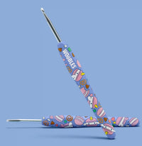The Woobles Bjorn the Narwhal: Sweetie Edition Crochet Kit features two beginner-friendly crochet hooks with light purple handles, charming yarn ball and treat designs, and "WOBBLES" printed on one handle against a light blue background.