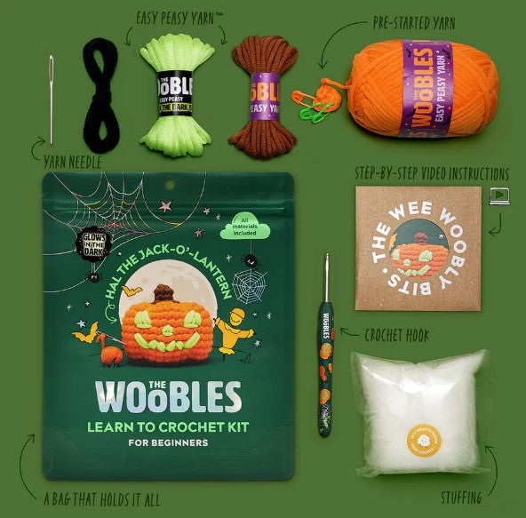The Woobles Hal the Jack-o-Lantern Crochet Kit for beginners is shown with orange, green, and black yarn, a crochet hook, yarn needle, stuffing, storage bag, video instructions, and a finished jack-o'-lantern sample.