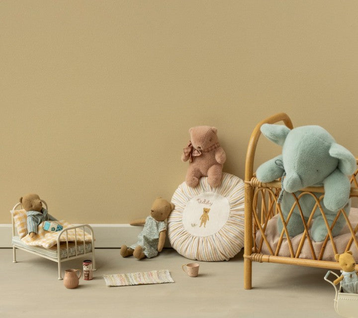 A Maileg Teddy bear plush, Mini - Vintage rose, along with a plush elephant, are arranged on toy beds and a cushion in a softly lit, minimalist children’s room featuring neutral hues, vintage rose accents, and simple Maileg-inspired decor.