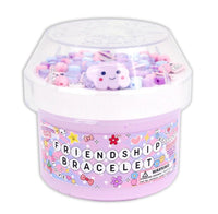 A pastel purple container labeled Dope Slime Friendship Bracelet by Dope Slime is filled with colorful beads and a smiling cloud charm, topped by a clear plastic lid. Perfect for sensory play, this fun item also has a visible warning label on the side.