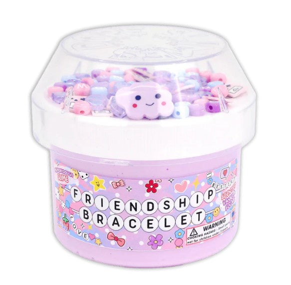 A pastel purple container labeled Dope Slime Friendship Bracelet by Dope Slime is filled with colorful beads and a smiling cloud charm, topped by a clear plastic lid. Perfect for sensory play, this fun item also has a visible warning label on the side.