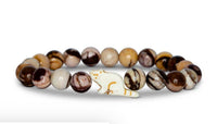 The fahlo Dash - Himalaya Stone Red Panda bracelet features round, marbled brown, tan, and cream beads with a central white cat-shaped bead with gold markings—ideal for wildlife conservation enthusiasts.
