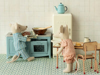 Two toy mice in pajamas enjoy imaginative play with the Maileg Kitchen, Mouse - Blue by Maileg, surrounded by dollhouse furniture as one mouse bakes and the other watches.